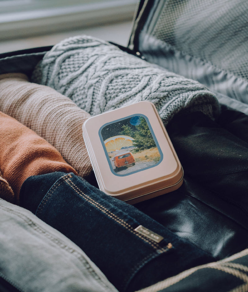 Van life travel tin in an open suitcase with dark and light jeans and pink and great sweaters