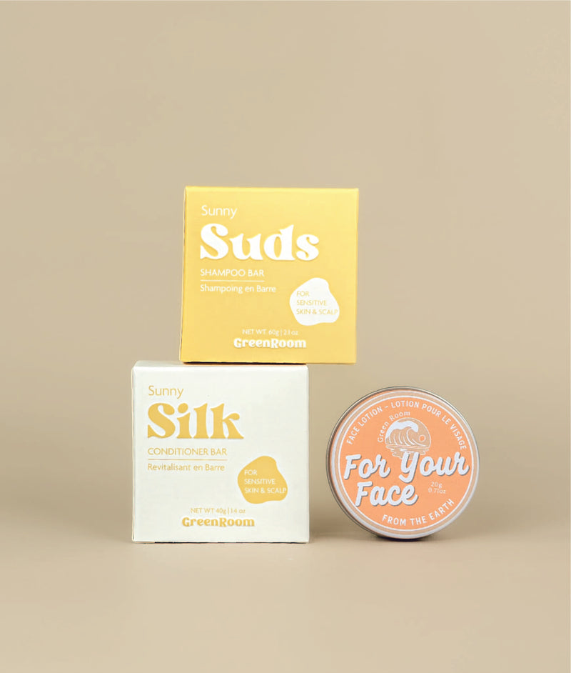 White with yellow writing sunny silk conditioner packing with the small yellow with white writing sunny suds shampoo bar packaging siting on top with a circular face lotion on its side to show orange label beside it