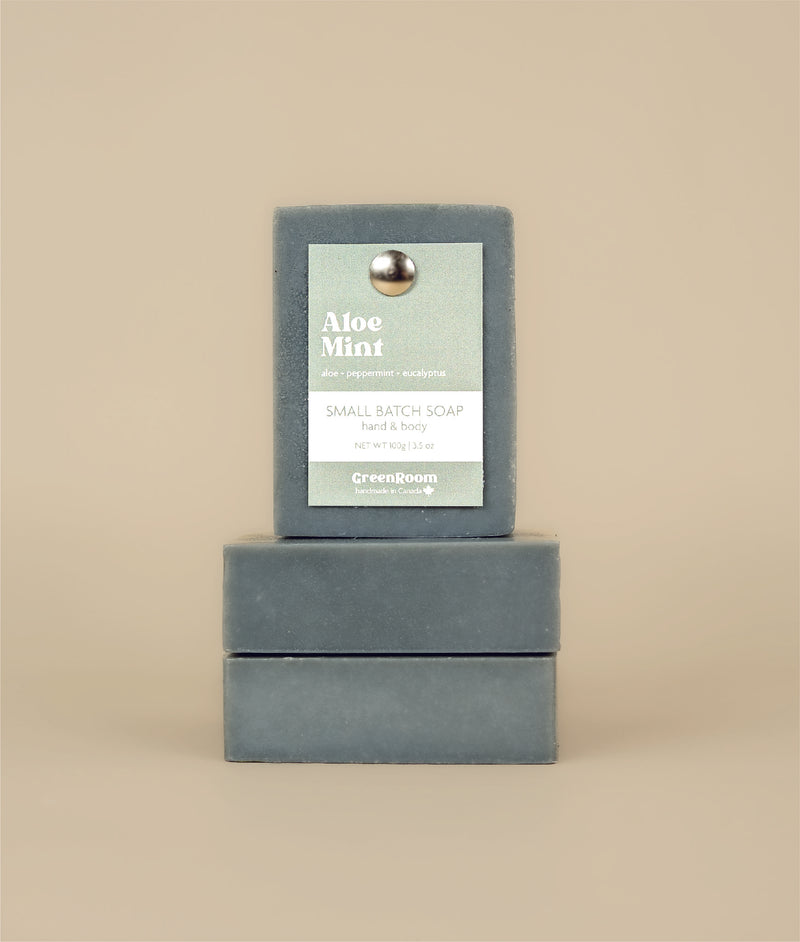 Two aloe mint soaps stacked on their sides with a aloe mint soap sitting on top with a recycled paper tag and metal push pin 