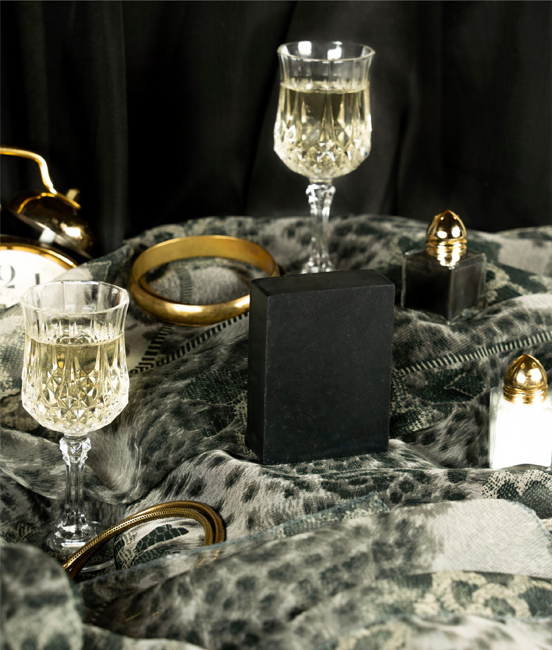 Charcoal and clay soap sitting on an animal print scarf with metal bangles, champagne in nice glasses and salt and pepper shakers around it 