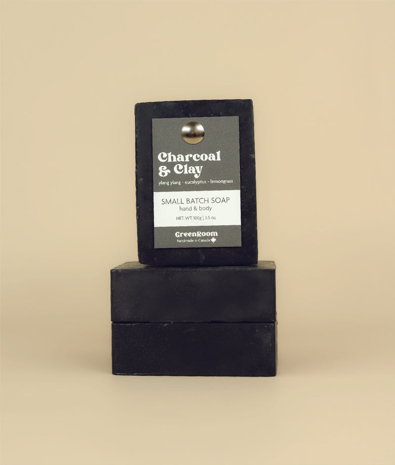 Two charcoal and clay soaps on their sides with a charcoal and clay soap sitting on top with a recycled paper tag held in by a metal push pin