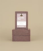 Two horizontally stacked lavender zinc soaps with a vertically stacked lavender zinc soap on top with a recycled paper purple tag held to the soap by a metal push pin 