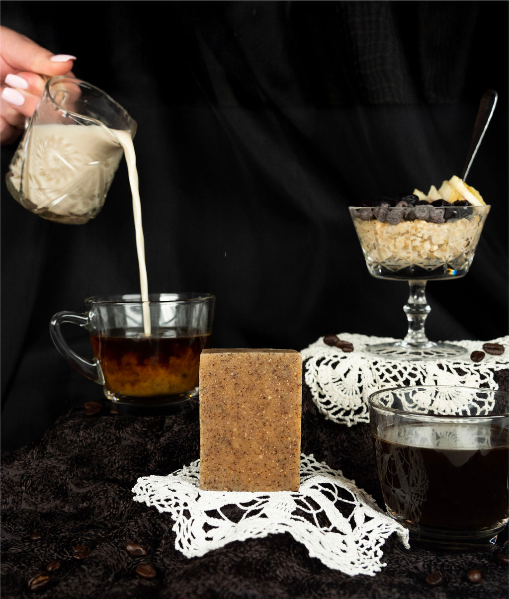 Oat milk latte soap sitting on a doily with milk being poured into coffee and a parfait behind it 