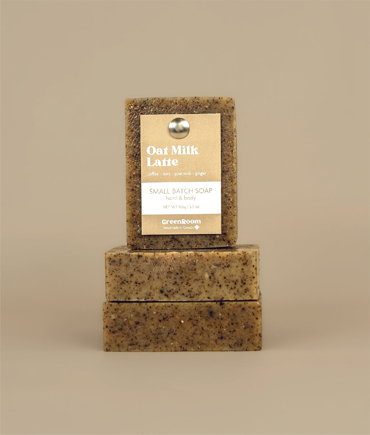 Two horizontal oat milk latte soaps stacked together with a certainly stacked oat milk latte soap with a recycled paper brown and white tag being held up by a metal push pin 