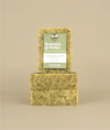 Two horizontally stacked seaweed and cedar soaps with a vertically placed seaweed and cedar soap on top with a green and white paper recycled tag held on by a metal push pin 