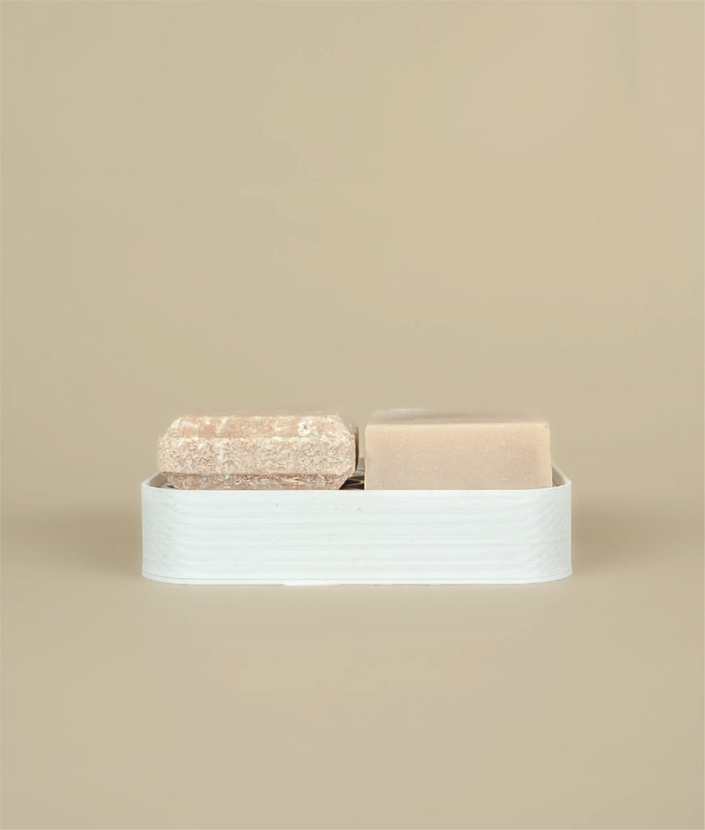 3D recycled plastic printed white soap dish With small pink floral suds and silk, shampoo and conditioner bars on top  of it